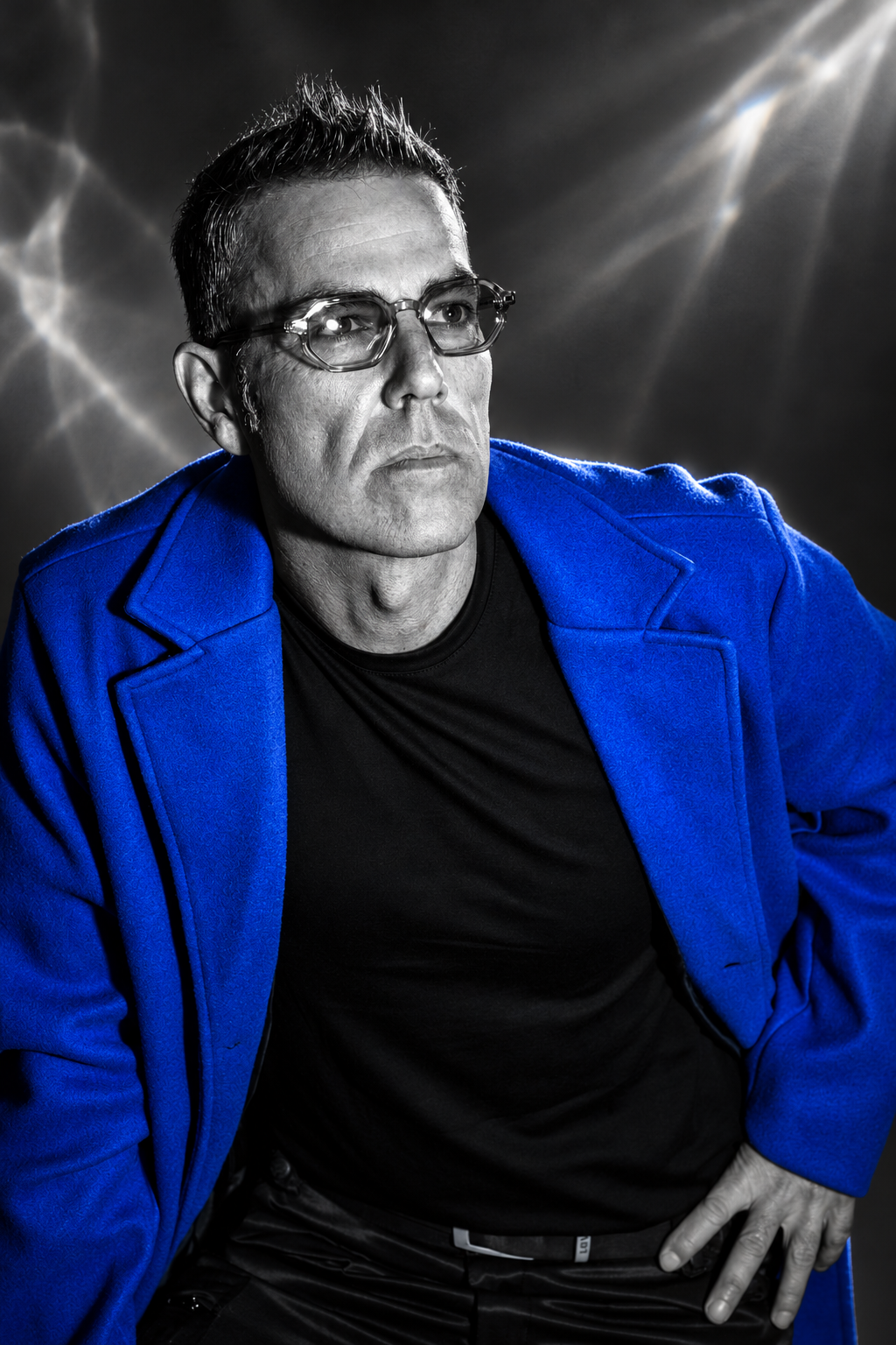Portrait de Yann Asahi en noir et blanc, manteau bleu électrique et faisceaux de lumière